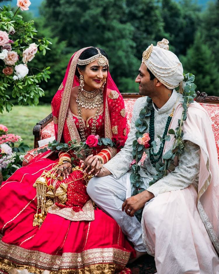 A bride and groom seated together beside a floral backdrop