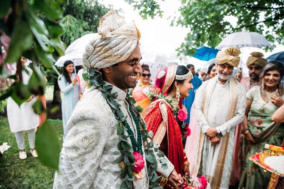 A groom in a garland of eucalyptus greeted by family