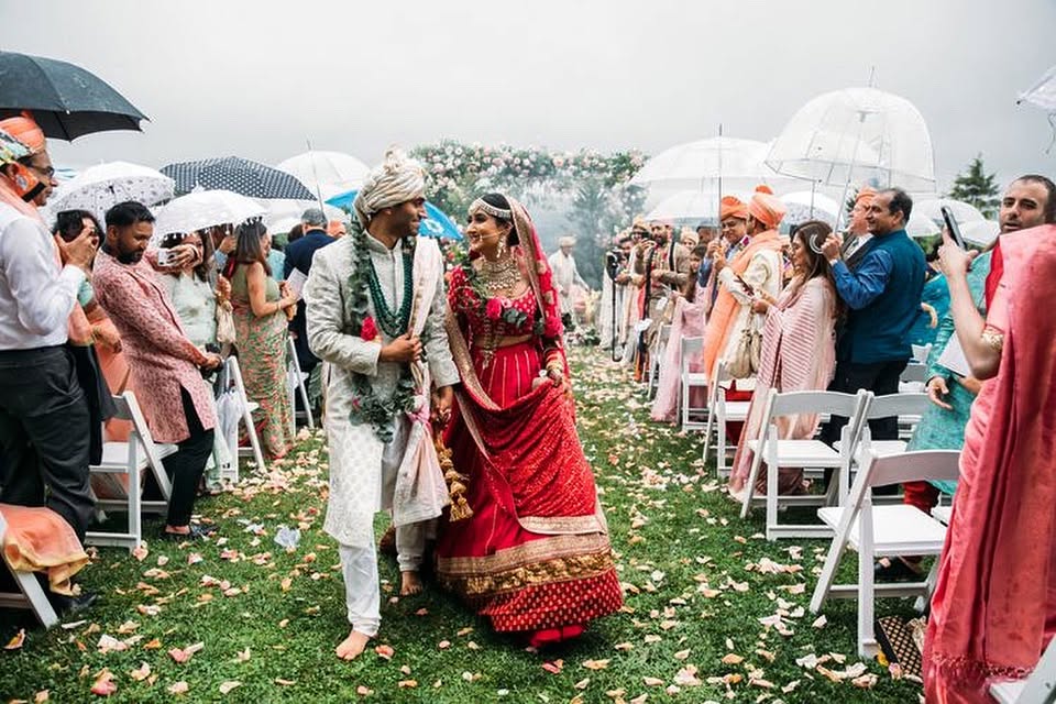 A Hindu bride and groom walking the petal aisle as guests hold parasols