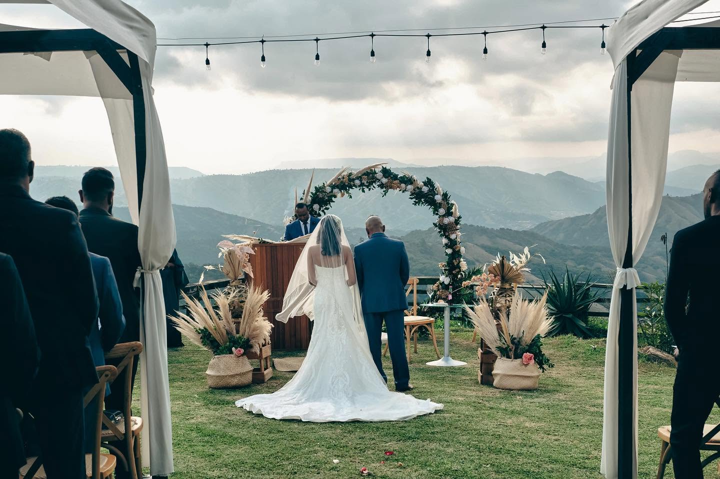 Guests watching a ceremony framed by draped poles and hills beyond