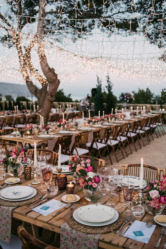Long tables set beneath string lights in the gardens at dusk