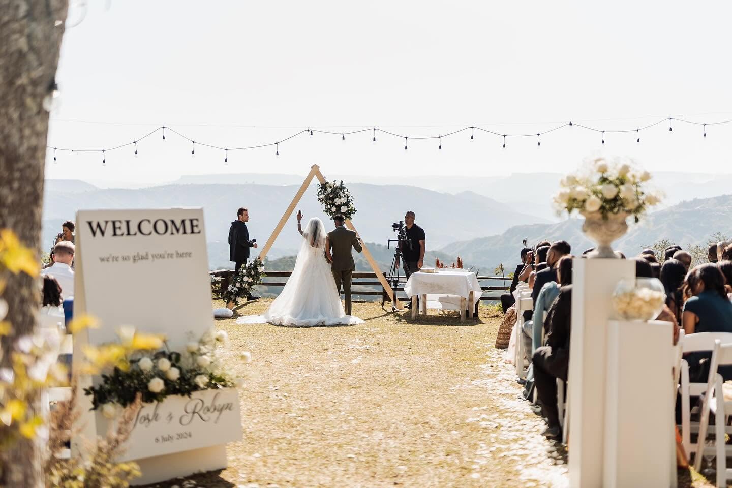 Ceremony beneath a timber triangle arch with string lights and valley views